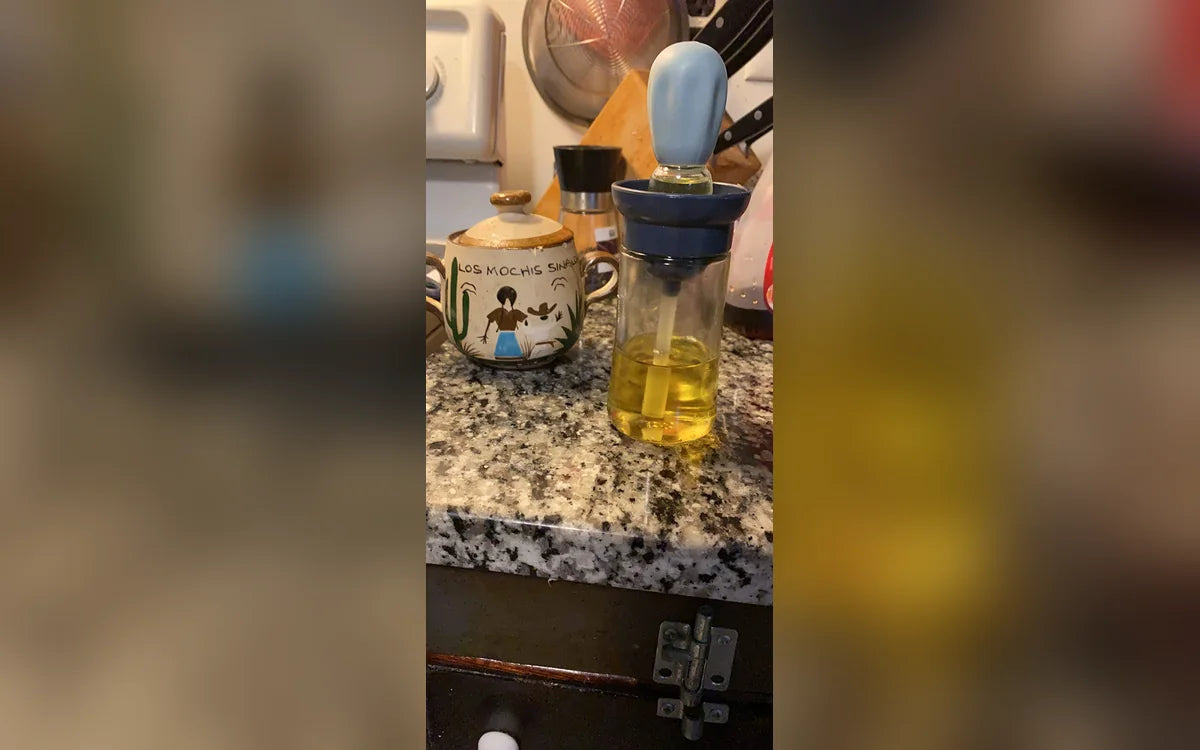 Aceitera azul con brocha integrada sobre un mesón de granito, foto de Carolina R.