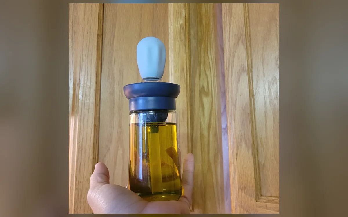 Aceitera de vidrio sostenida frente a un gabinete de cocina, foto de Mónica L.